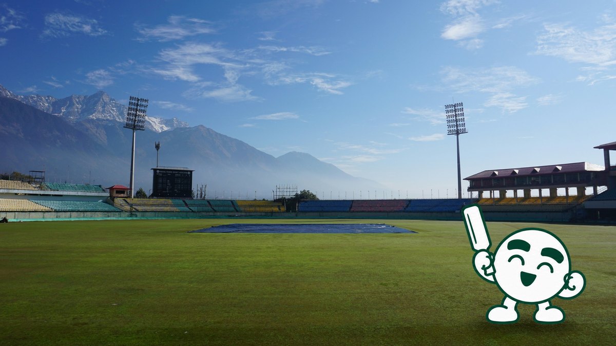 An empty cricket ground in Dharamshala with mountains behind and covers on the pitch.