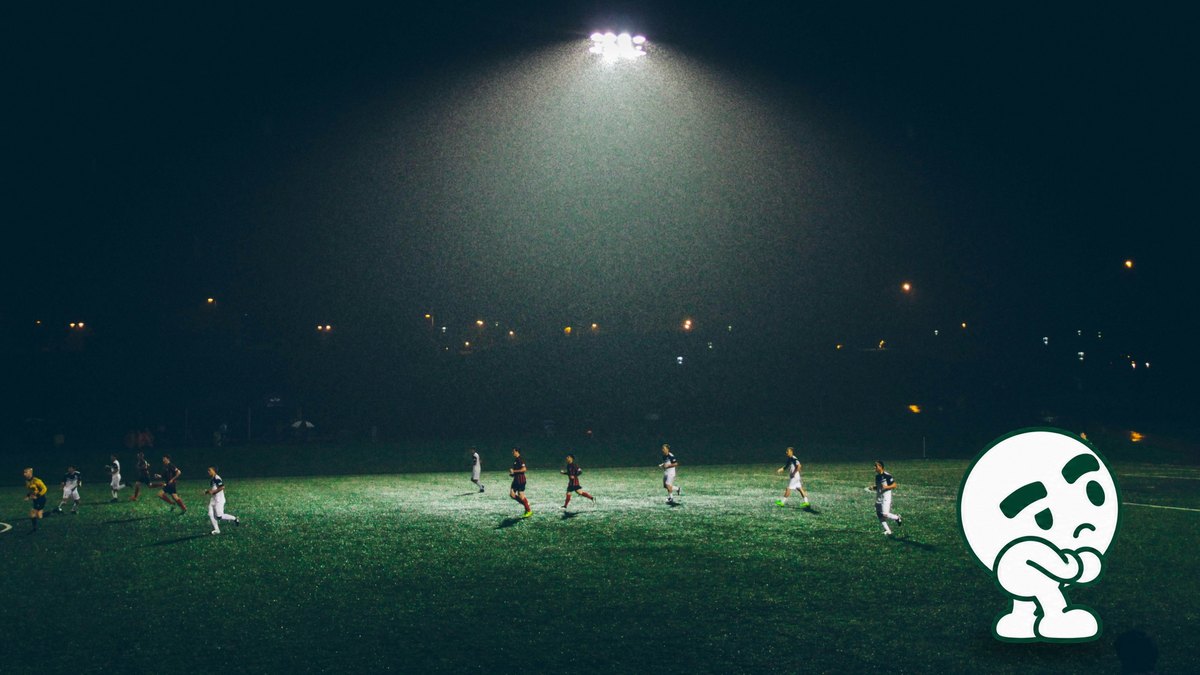 Players on a football pitch at night under a single floodlight.